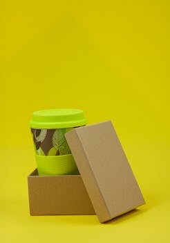 Isolated eco friendly box with lid containing disposable green cup on yellow background